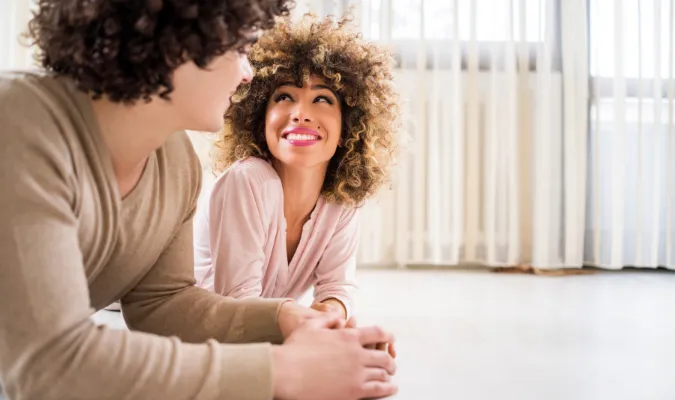 A black woman wearing a light pink shirt and a person who appears to be a white male wearing a beige sweater are creating connection in their relationship. 
