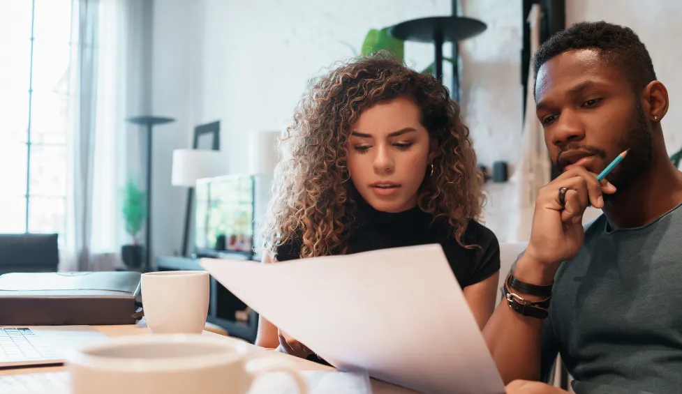 A black woman with long hair wearing a black shirt and a black man with short hair and a short beard wearing a gray shirt are journaling together to work on their relationship.