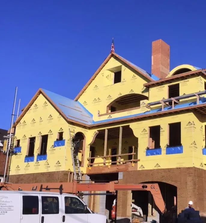 Partially constructed house covered in yellow paper with GP logo, metal support poles, and a white work van parked in front.