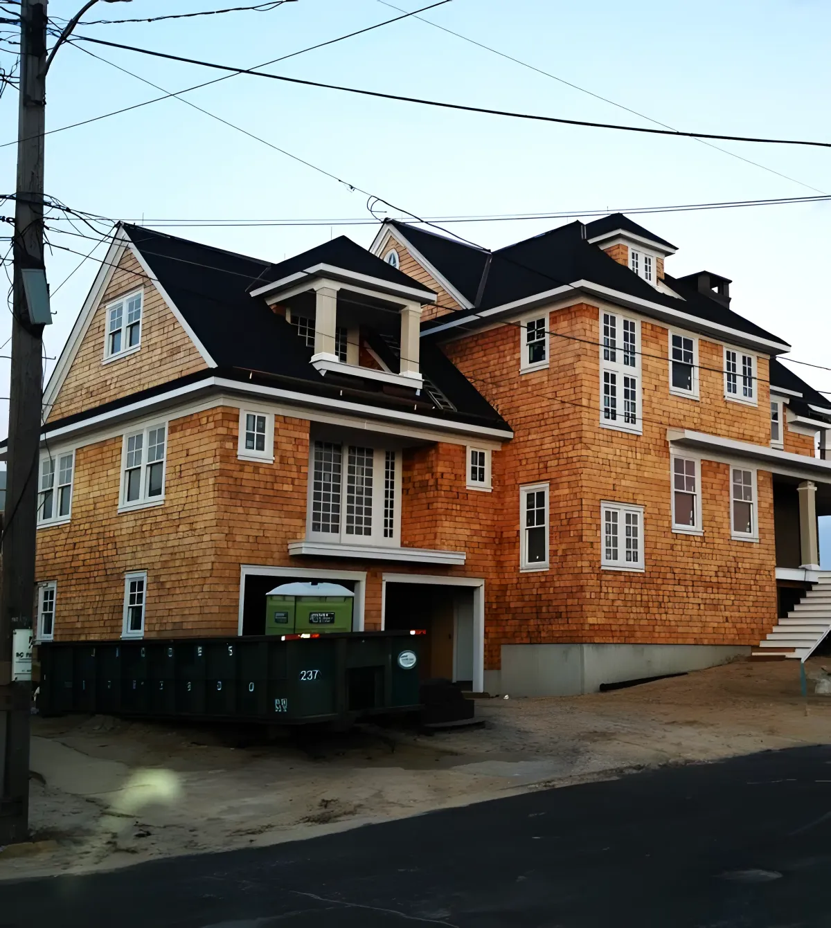 Elegant finished brick house featuring a black roof and a garage, adorned with multiple windows and stairs leading up to a welcoming deck.