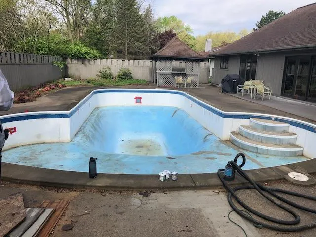 Drained residential inground pool with an old, stained, and faded pool liner before replacement by Fizer Pools in Rockford, MI