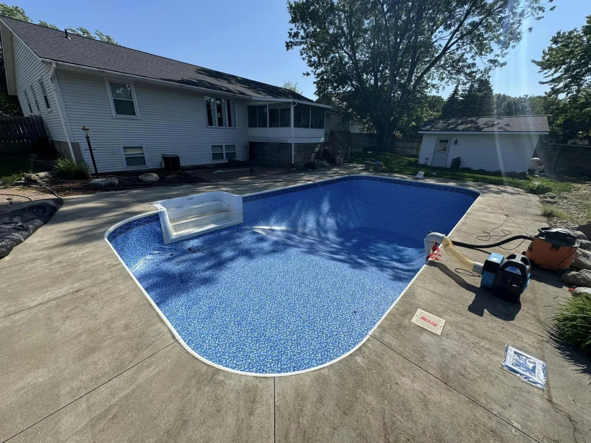 Backyard inground pool featuring a vibrant blue vinyl liner and concrete deck