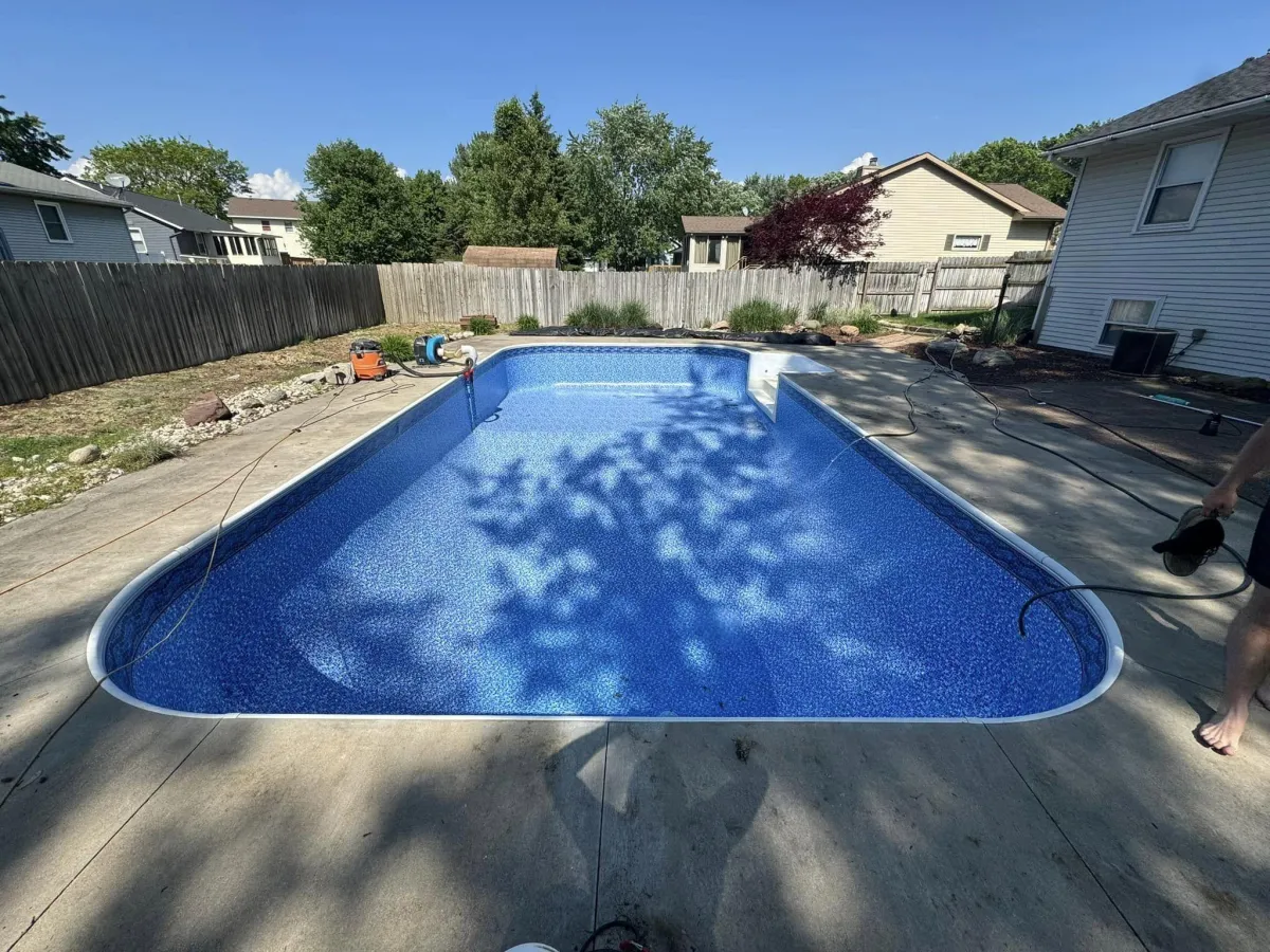 Finished pool liner replacement showing sparkling clear blue water and surrounding concrete patio by Fizer Pools.