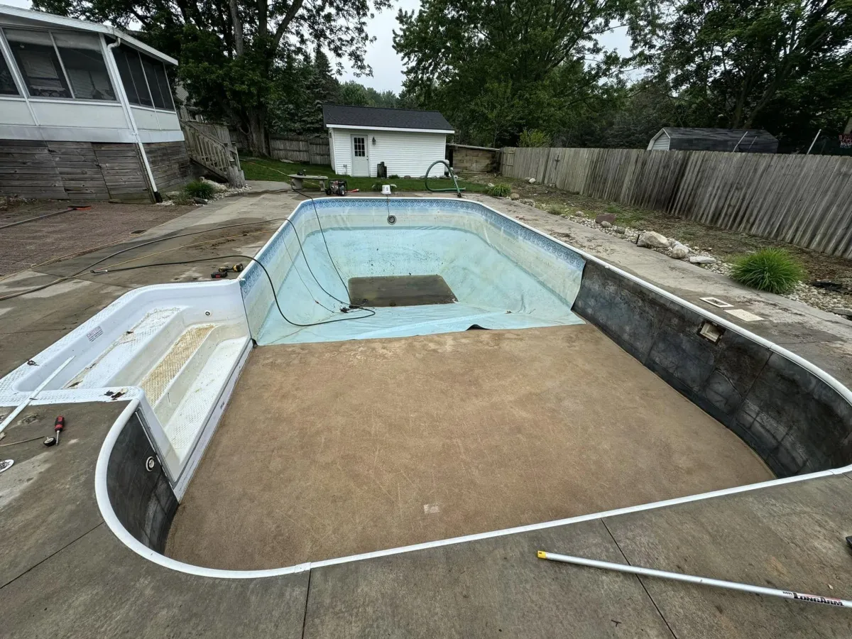 In-progress backyard pool restoration showing a fully drained inground pool cavity prepped for a new liner by Fizer Pools.