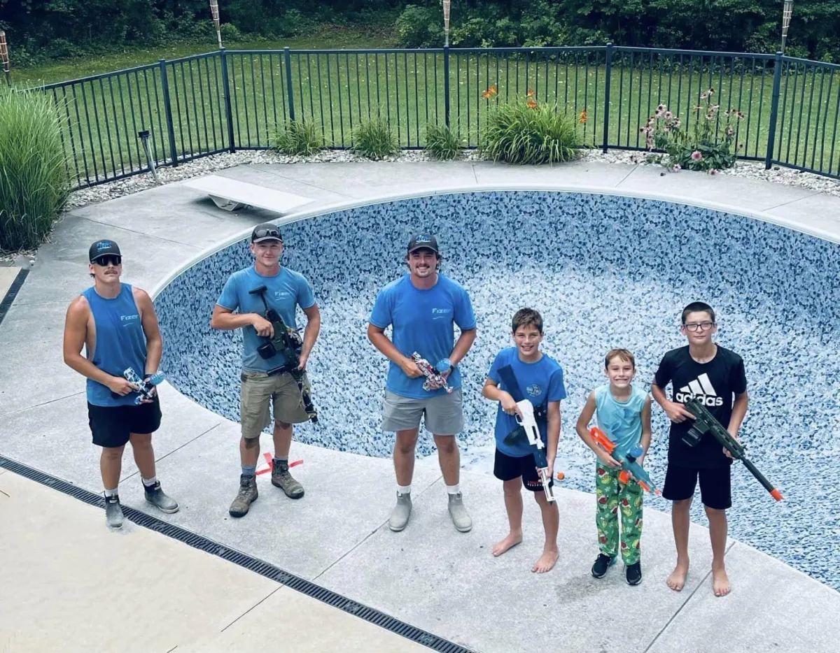 Fizer Pools installation team and kids posing with toy Nerf blasters next to a newly lined inground pool in Ada, MI