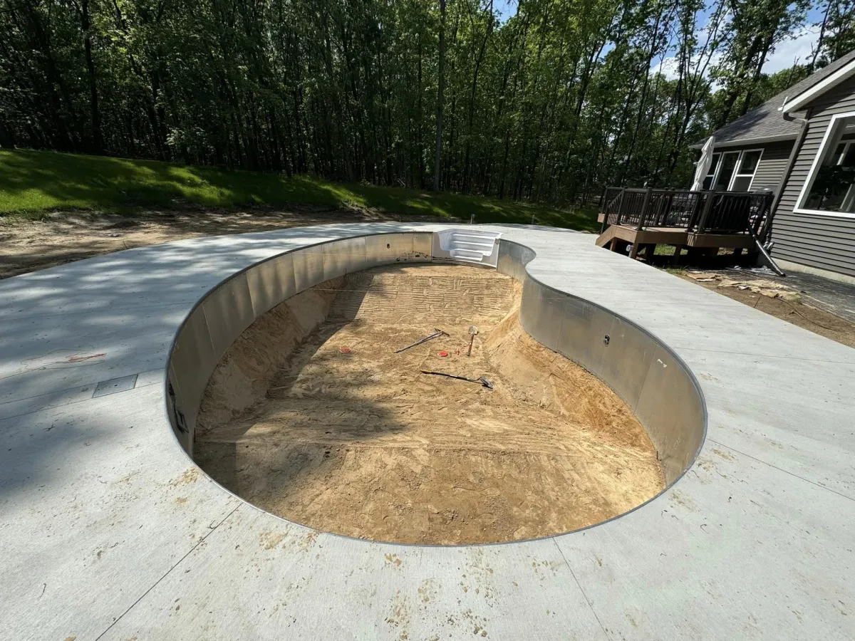 Groundwork phase of an inground swimming pool installation showing the excavated dirt hole and concrete pool deck surround by Fizer Pools.