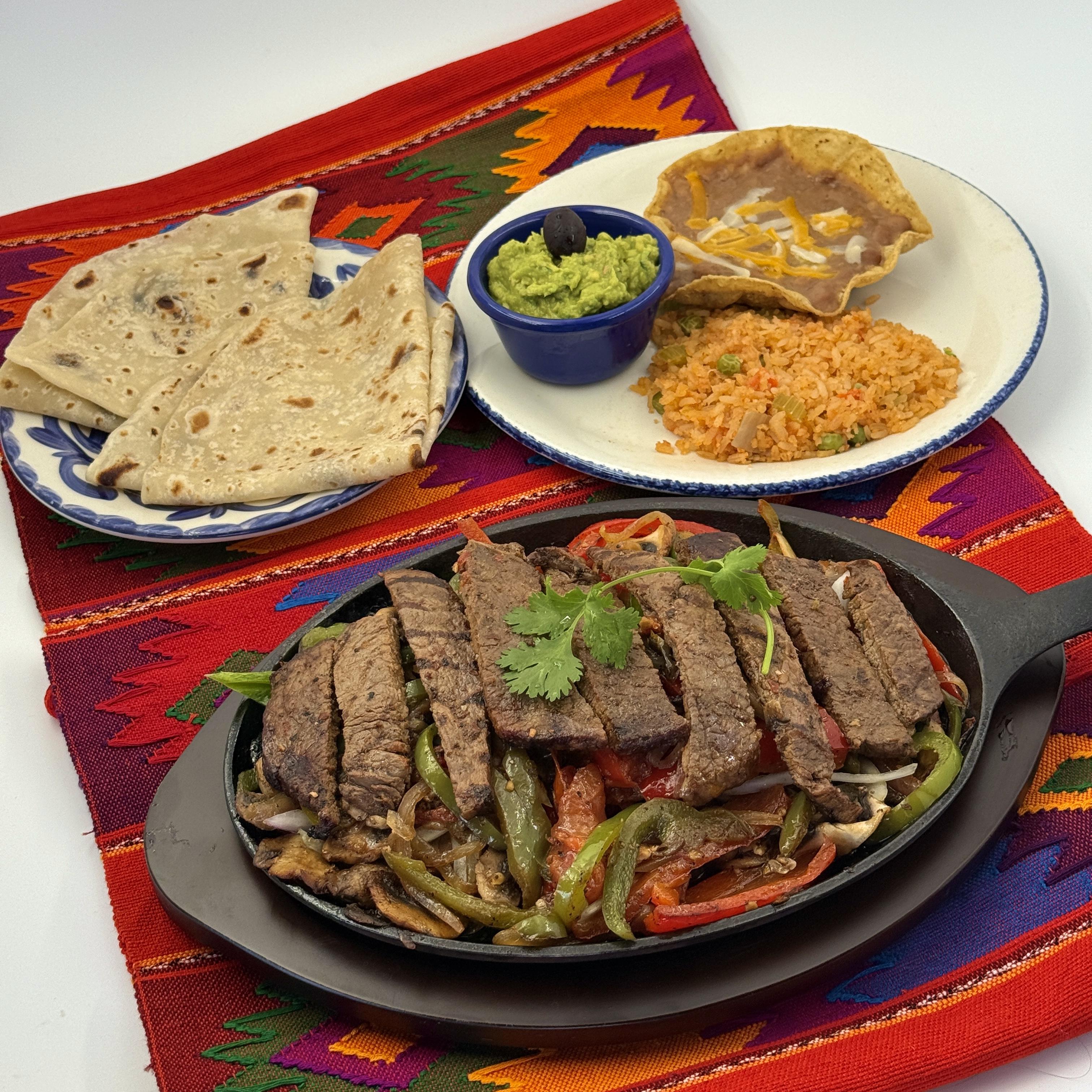 Beef Fajitas-Flame-grilled Carne Asada with fresh bell peppers mushrooms, onions, and tomatoes on a sizzling skillet. Served with frijoles de la olla, guacamole, and Arroz Mexicano broth.