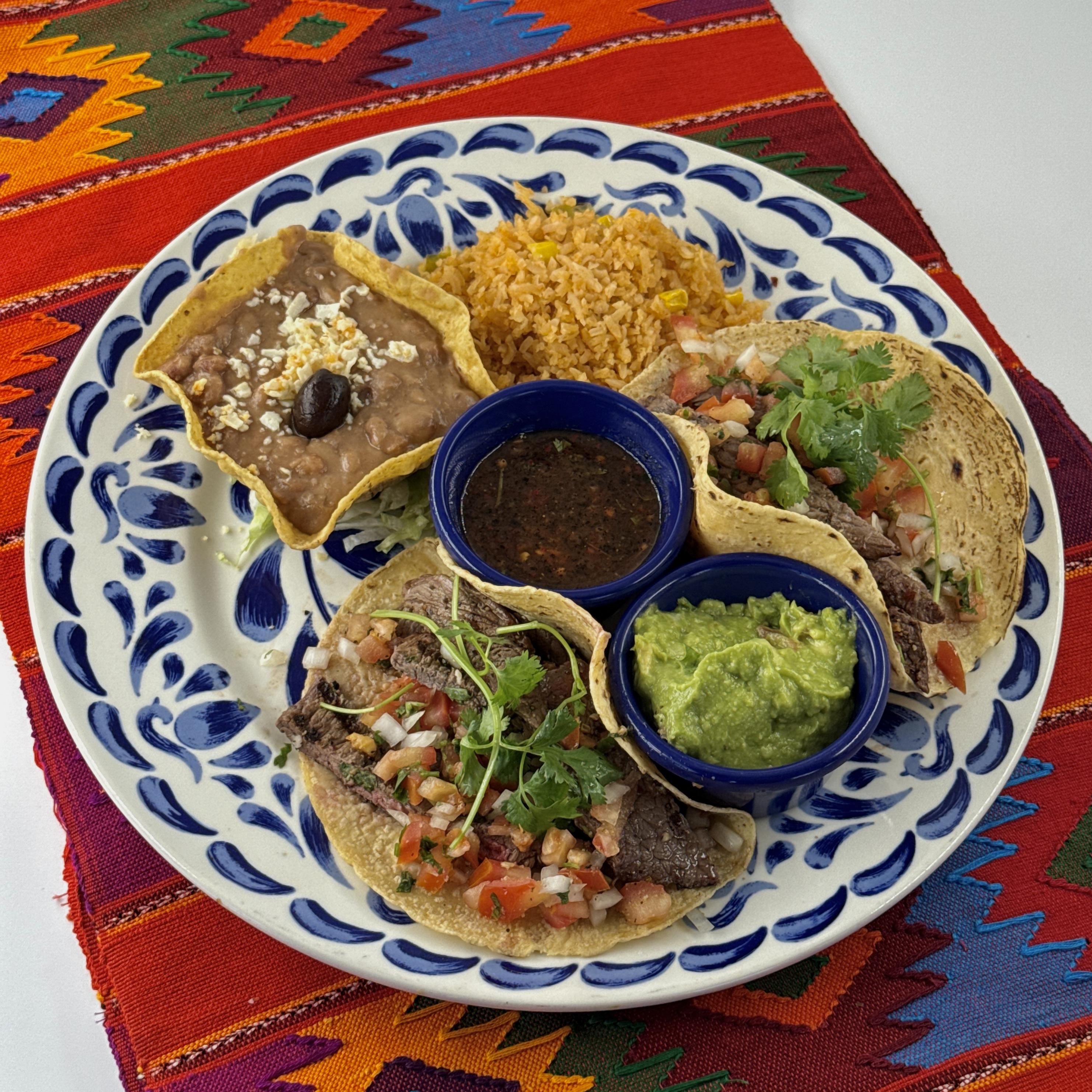 Carne Asada Tacos, Juicy sliced carne asada in two large tacos with guacamole, pico de gallo, salsa quemada, Pico beans and rice.