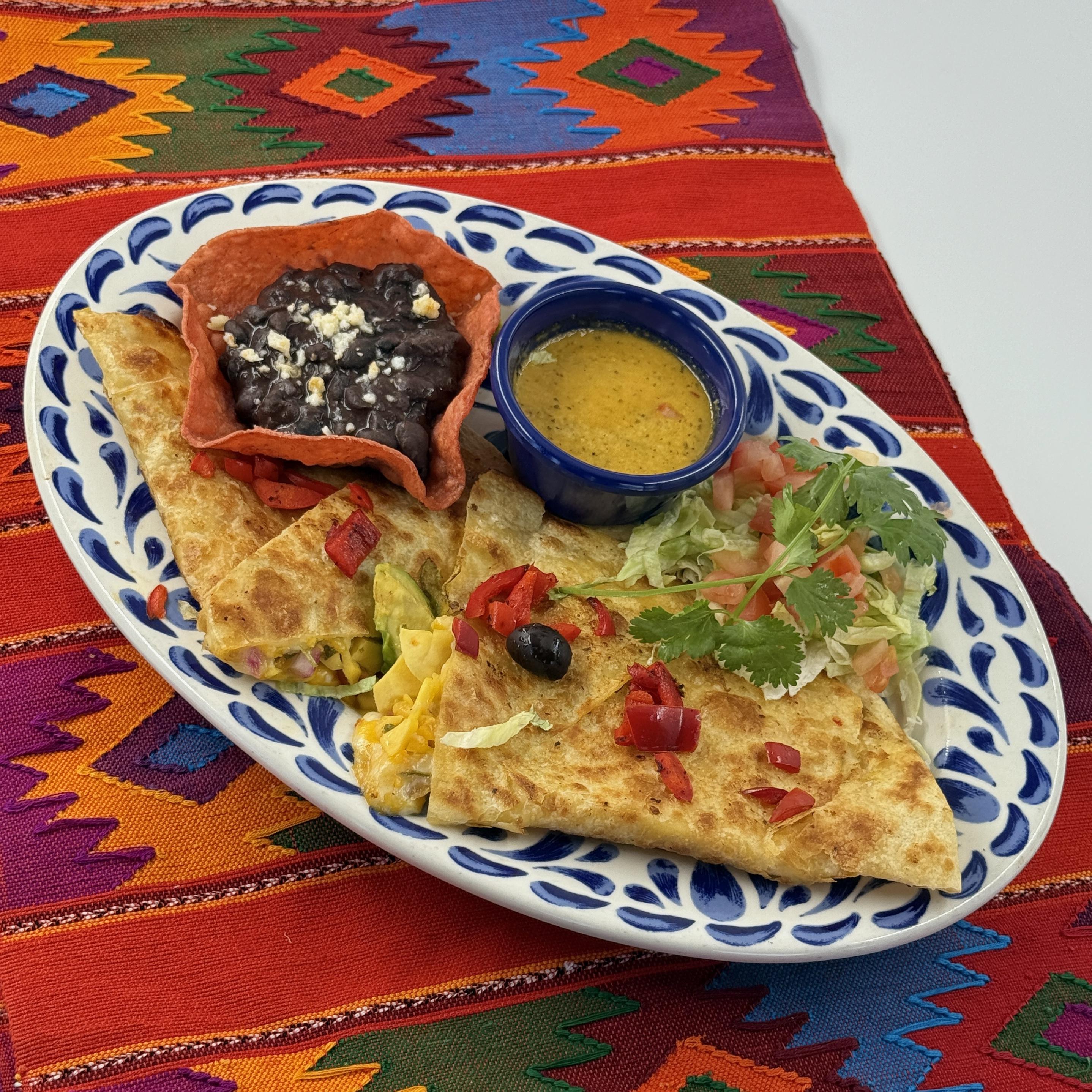 AVOCADO, MANGO & RED PEPPER QUESADILLA, A flavorful quesadilla made with a flour tortilla filled with two cheeses, avocado, mango and roasted red pepper. Served with a concha of black beans..