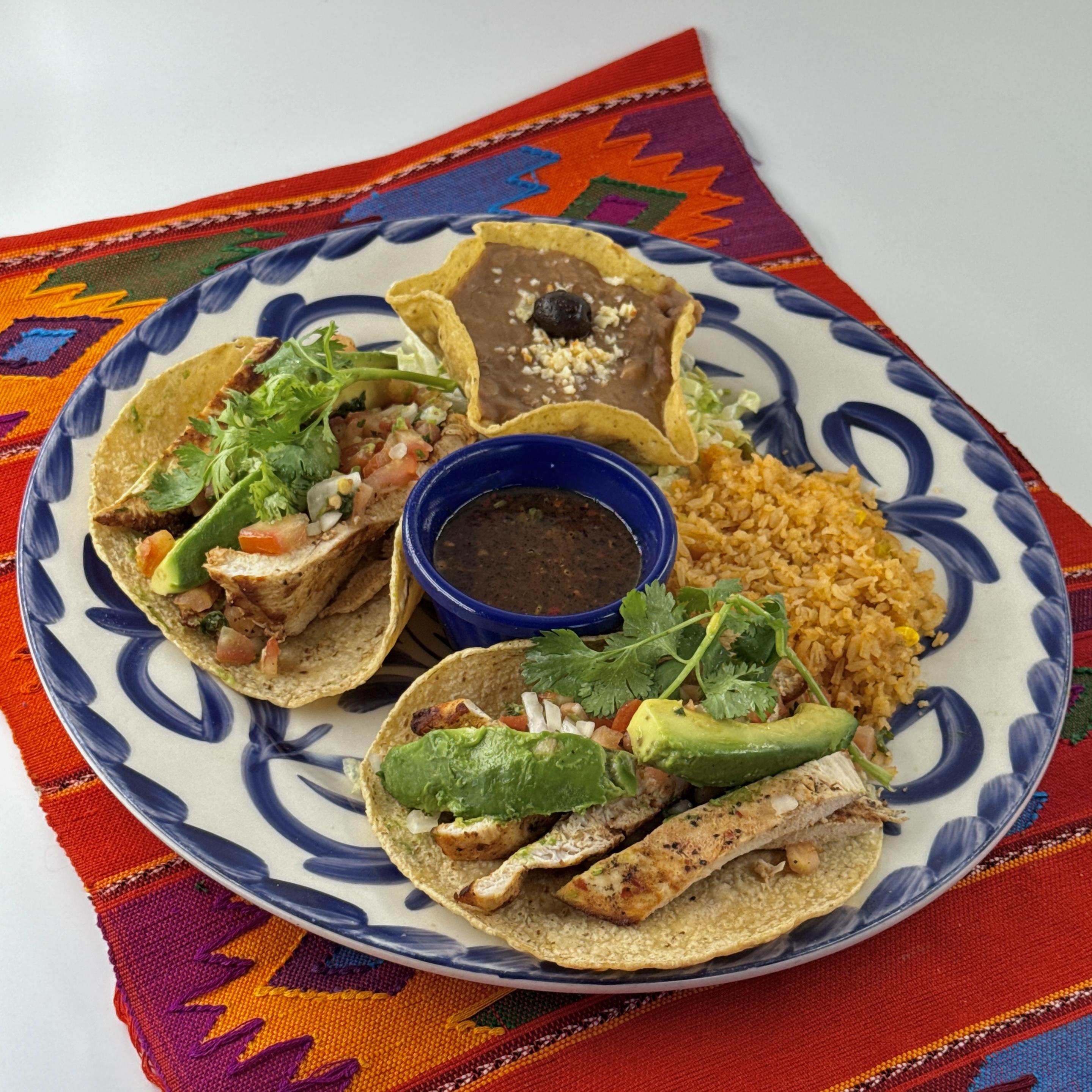 Chicken & Avocado Tacos, Two soft corn tortillas filled with seasoned strips of grilled chicken breast, sliced avocados and served with salsa quemada, rice and beans.