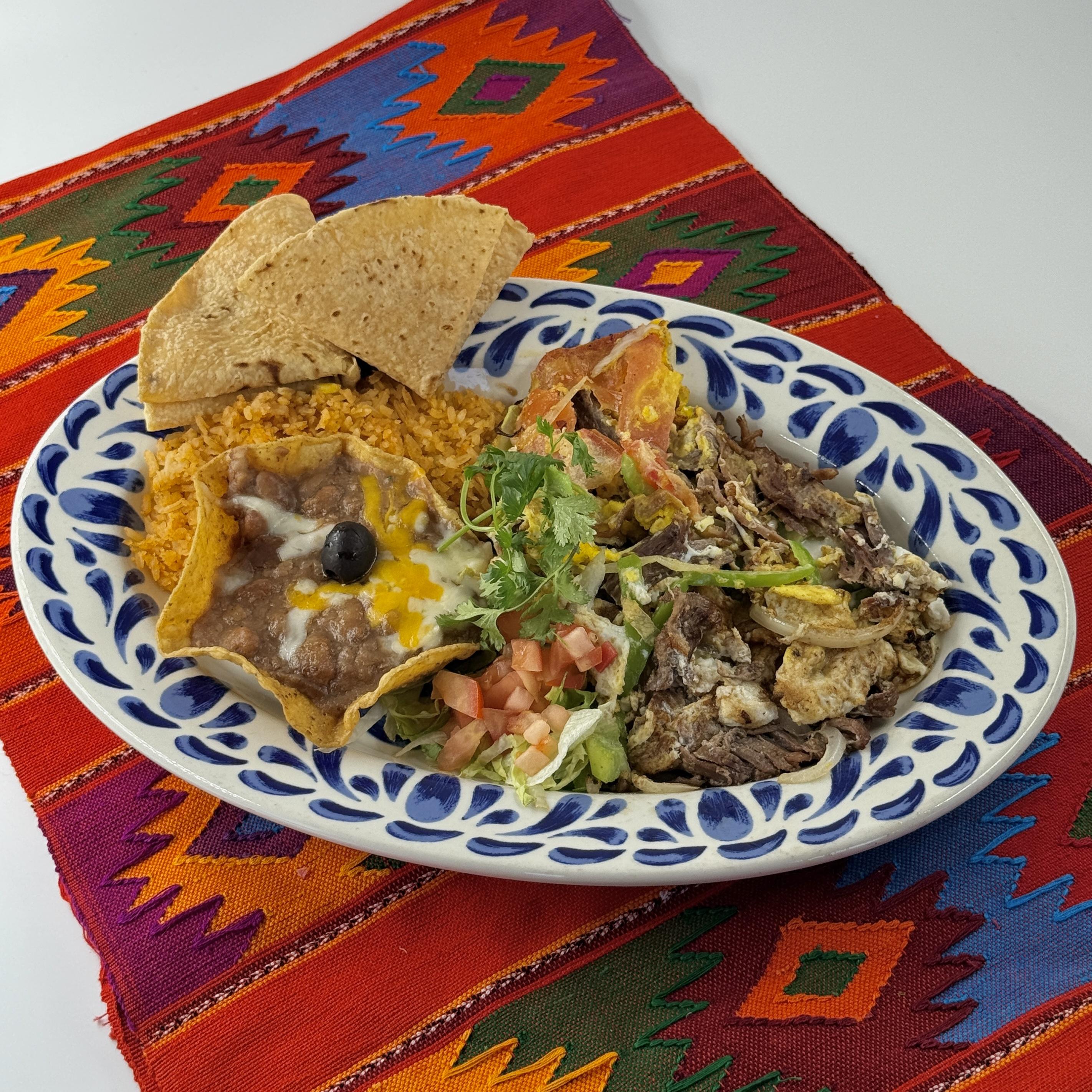 Machaca Traditional Machaca. This hearty breakfast features Shredded Beef, tender and flavorful, scrambled together with fresh Eggs. We add Tomatoes, Mild Peppers, and Onions into the mix, their vibrant flavors adding a refreshing contrast to the rich beef and eggs.