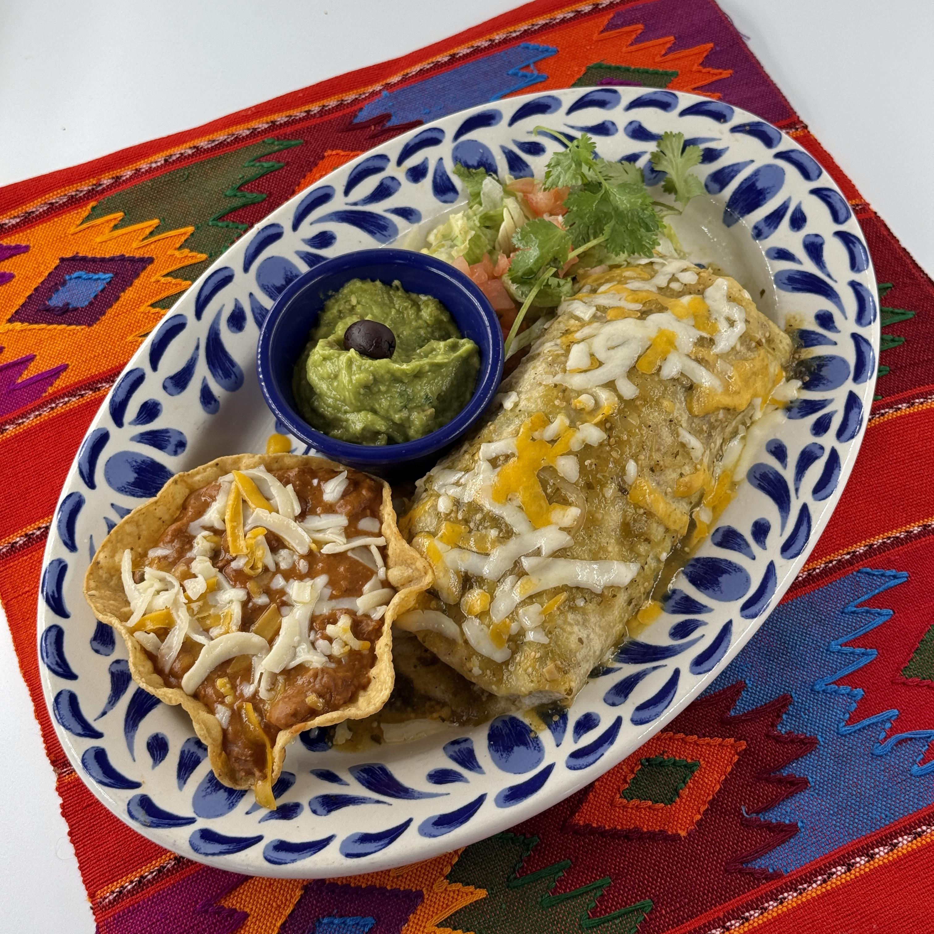 Grilled Carnitas Burrito, A flour tortilla filled with grilled carnitas, grilled onions and fresh grilled serrano chile slices. Topped with green tomatillo sauce and melted cheese. With Pico beans and guacamole.