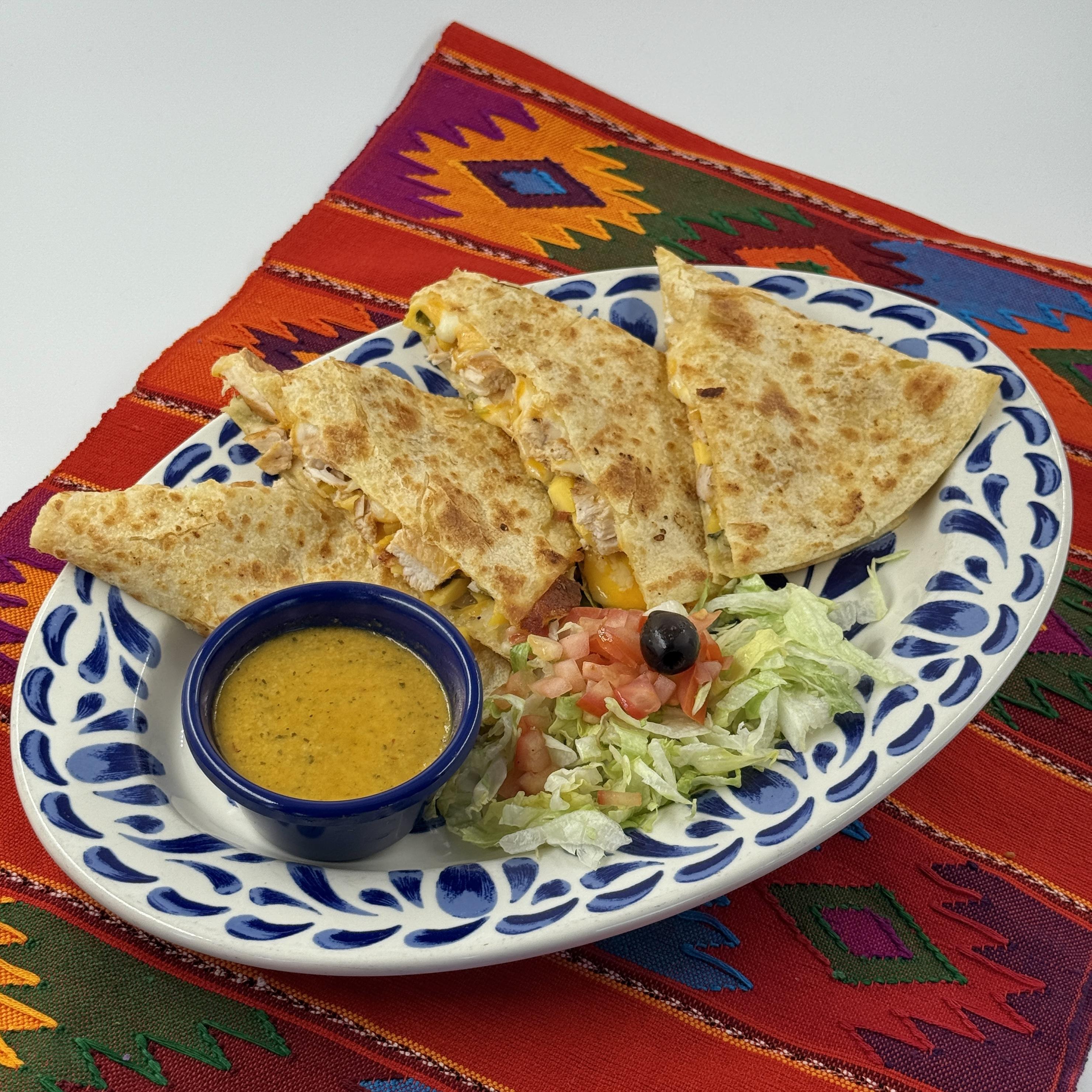 GRILLED CHICKEN & MANGO QUESADILLA, Tender grilled chicken and sweet juicy mango chunks nestled in a warm, soft handmade flour tortilla, bursting with a savory-sweet flavor blend, drizzled and served alongside zesty mango chipotle sauce.