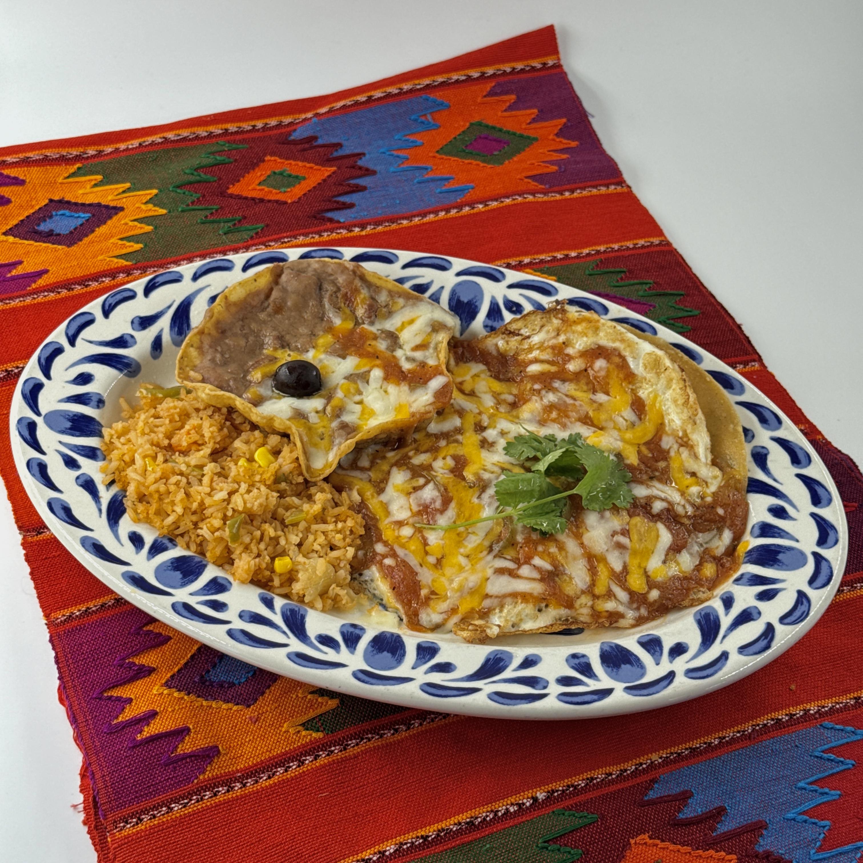 Huevos Rancheros,Experience the authentic charm of Mexican mornings with our "Huevos Rancheros". Savor the delight of lightly fried eggs nestled on a bed of crispy corn tortillas, bathed in an exquisite salsa española that lends a vibrant tang. This symphony of flavors is crowned with a generous layer of perfectly melted cheese, adding a creamy richness that will make your taste buds dance. Accompanied by our traditional Mexican rice and refried beans, this dish is a hearty start to your day. And to complete the experience, we serve it with hot, fresh tortillas - a soft, warm hug for your palette. Welcome the day with this comforting feast, a true homage to the heart of Mexico.