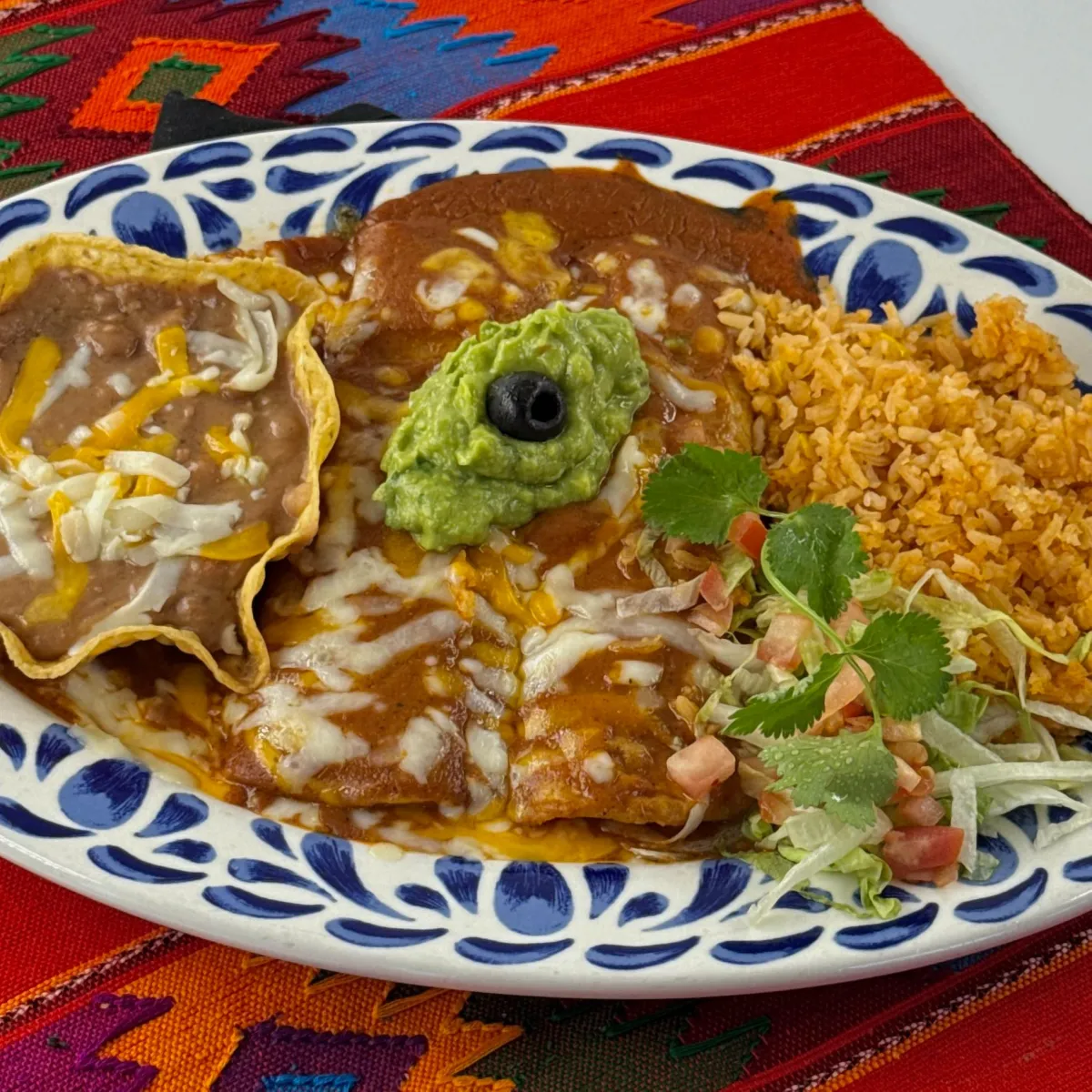 Enchiladas topped with guacamole and sour cream with rice and beans