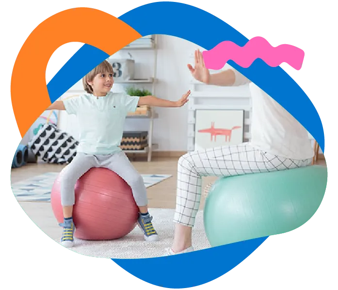 Occupational therapist kneeling at child height and guiding a small child with blocks in a bright therapy room.