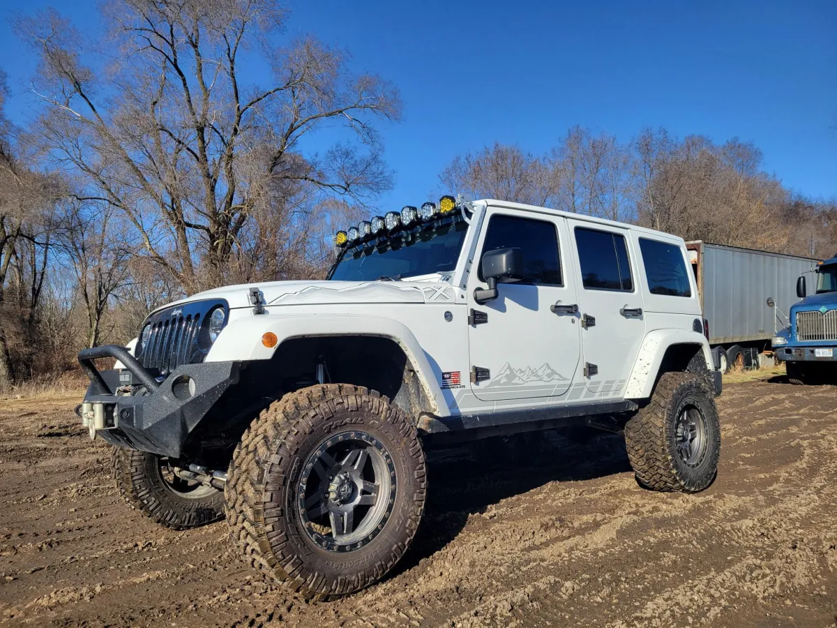 A modified white Jeep Wrangler parked in a rural Michigan field, showcasing a high-performance suspension system and off-road tires.