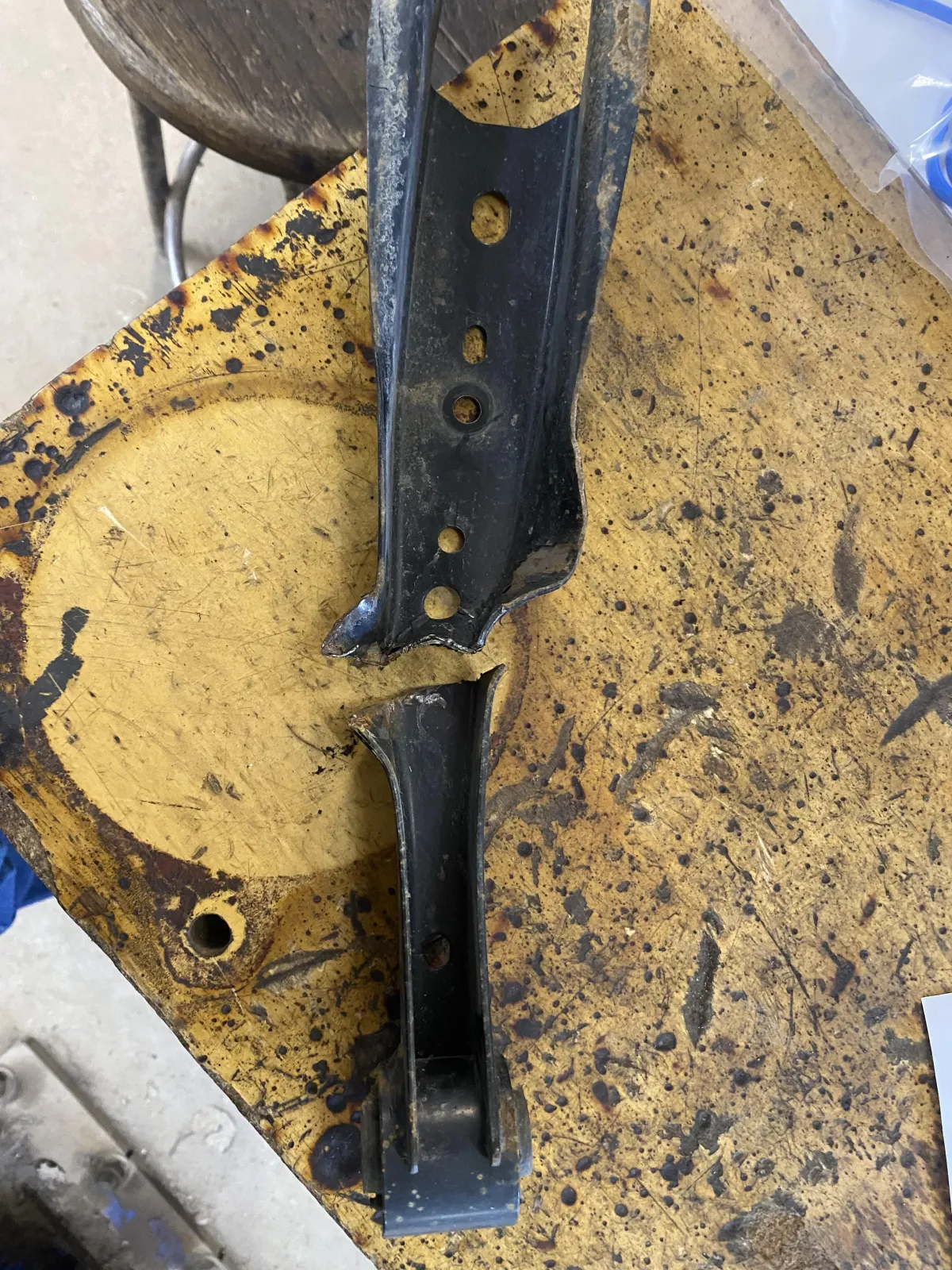 A close-up of a broken and rusted metal suspension control arm resting on a yellow workbench at Wilder's Tire & Auto Service.