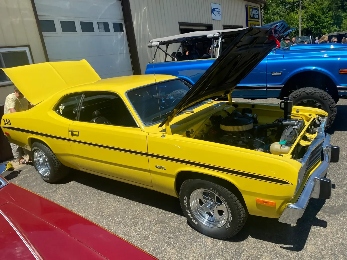Classic yellow 1970s Plymouth Duster with its hood propped open at an auto repair shop