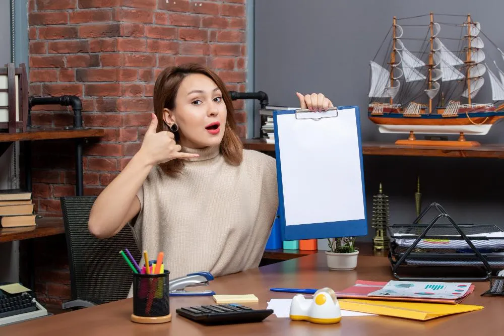 Woman gesturing phone call and holding blank clipboard in office, encouraging consultation and connection