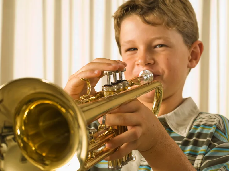 Two children playing an upright piano together, one focusing on the lower keys and the other on the higher ones. Both kids are smiling, engaged in playing, in a cozy room with warm lighting. The scene highlights the joy of collaborative music-making.