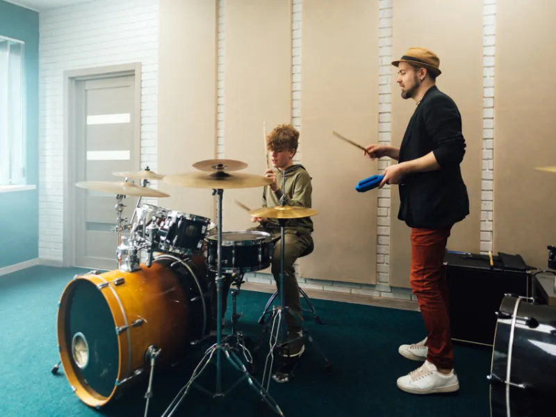 Two children playing an upright piano together, one focusing on the lower keys and the other on the higher ones. Both kids are smiling, engaged in playing, in a cozy room with warm lighting. The scene highlights the joy of collaborative music-making.