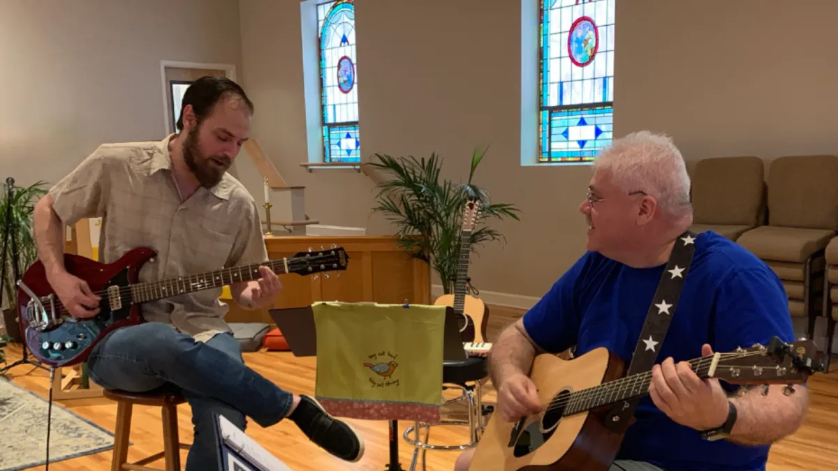 An adult, dressed in a colorful long sleeve and eyeglasses, sits attentively at a sleek digital keyboard, their fingers moving gracefully over the keys. The soft glow of a tilt light bathes the scene, casting an inviting, warm ambiance around them. 