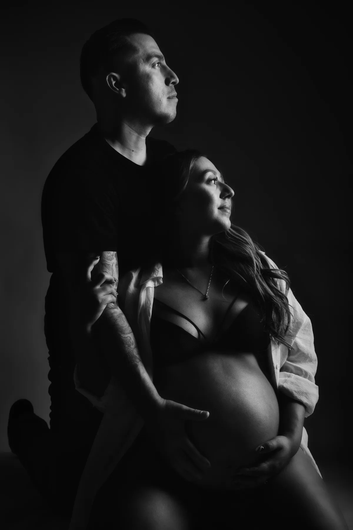pregnancy woman sitting holding her belly with her significant other holding her belly also