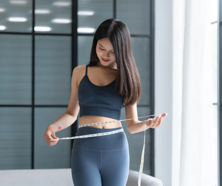 Woman measuring weight loss progress with tape measure at waist