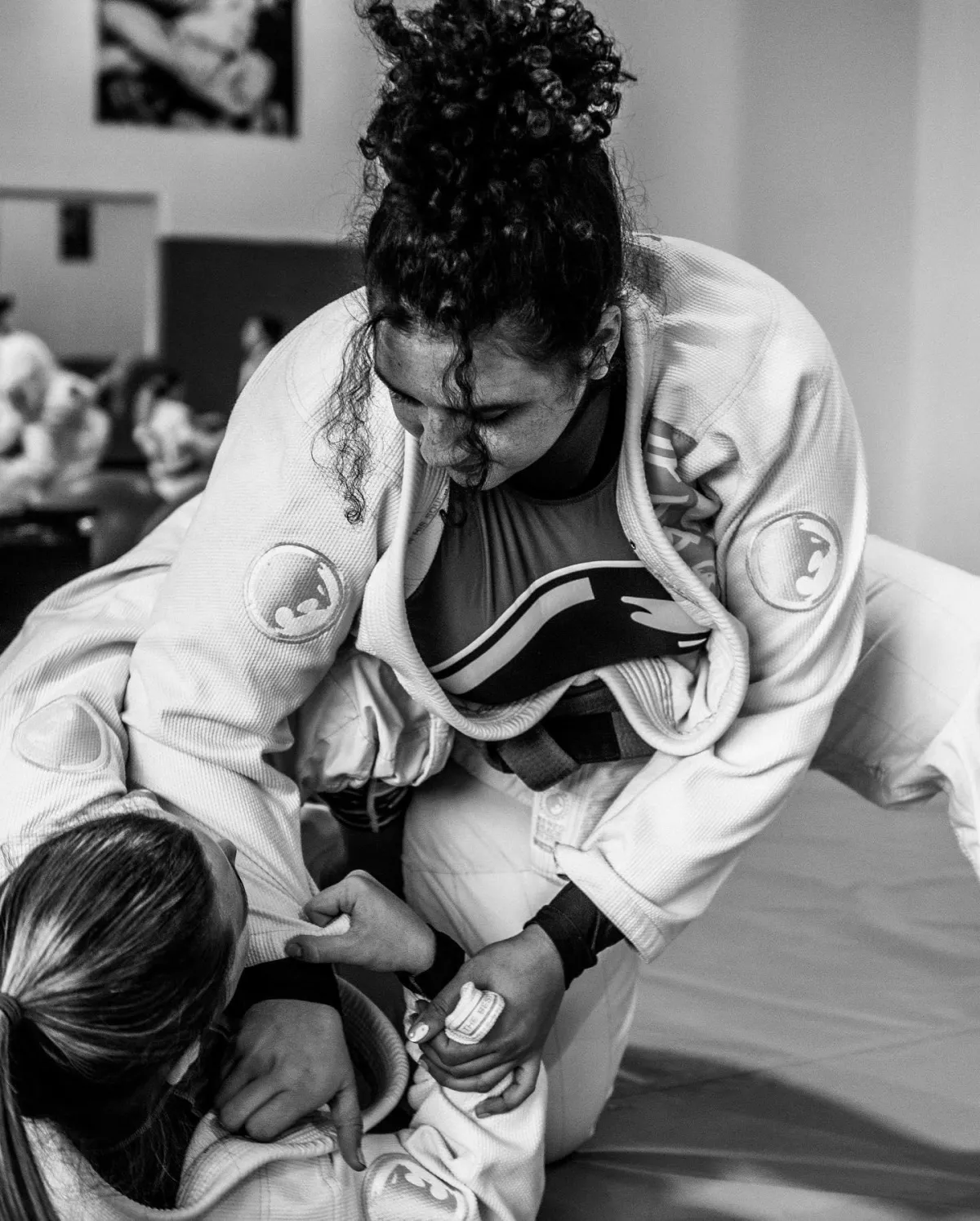 The image shows two women grappling with each other on the mat at the Renzo Gracie Academy of Jiu-Jitsu in Lake Worth. The women are wearing traditional jiu-jitsu uniforms (gi) and are fully engaged in their practice session. They are using a combination of grappling and groundwork techniques as they refine their jiu-jitsu skills. The gym has a spacious and well-lit training area, with mats covering the floor and motivational posters and banners on the walls. The atmosphere is one of discipline and concentration, as the women work to improve their jiu-jitsu proficiency. The image represents the inclusive and diverse community at the Renzo Gracie Academy, where women are encouraged and empowered to pursue their passion for martial arts.