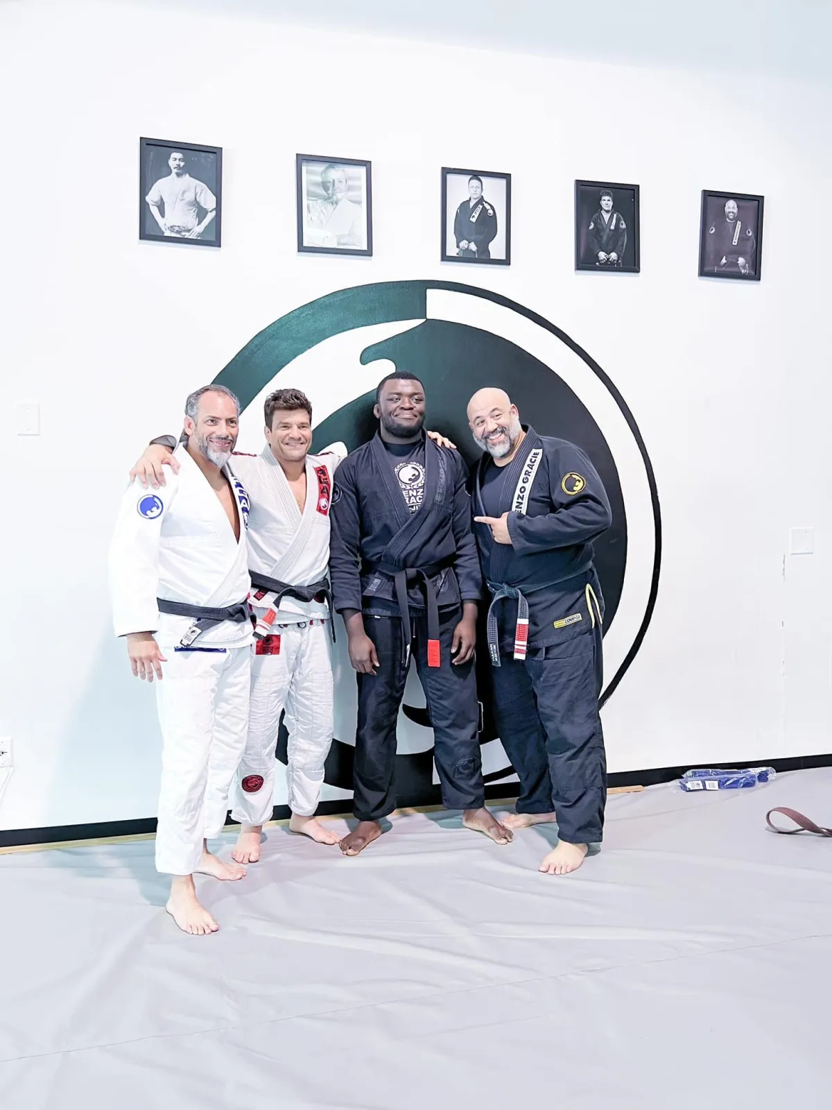 two of the instructors at the Renzo Gracie Academy of Lake Worth, along with a guest instructor named Stan Beck. The three men are standing in front of the Renzo Gracie of Lake Worth logo, which is displayed on a wall behind them. The instructors are wearing traditional jiu-jitsu uniforms (gi) and black belts, and they are smiling for the camera. The gym has a spacious and well-lit training area, with mats covering the floor and motivational posters and banners on the walls. The image represents the sense of community and dedication to excellence in jiu-jitsu training that the Renzo Gracie Academy embodies.