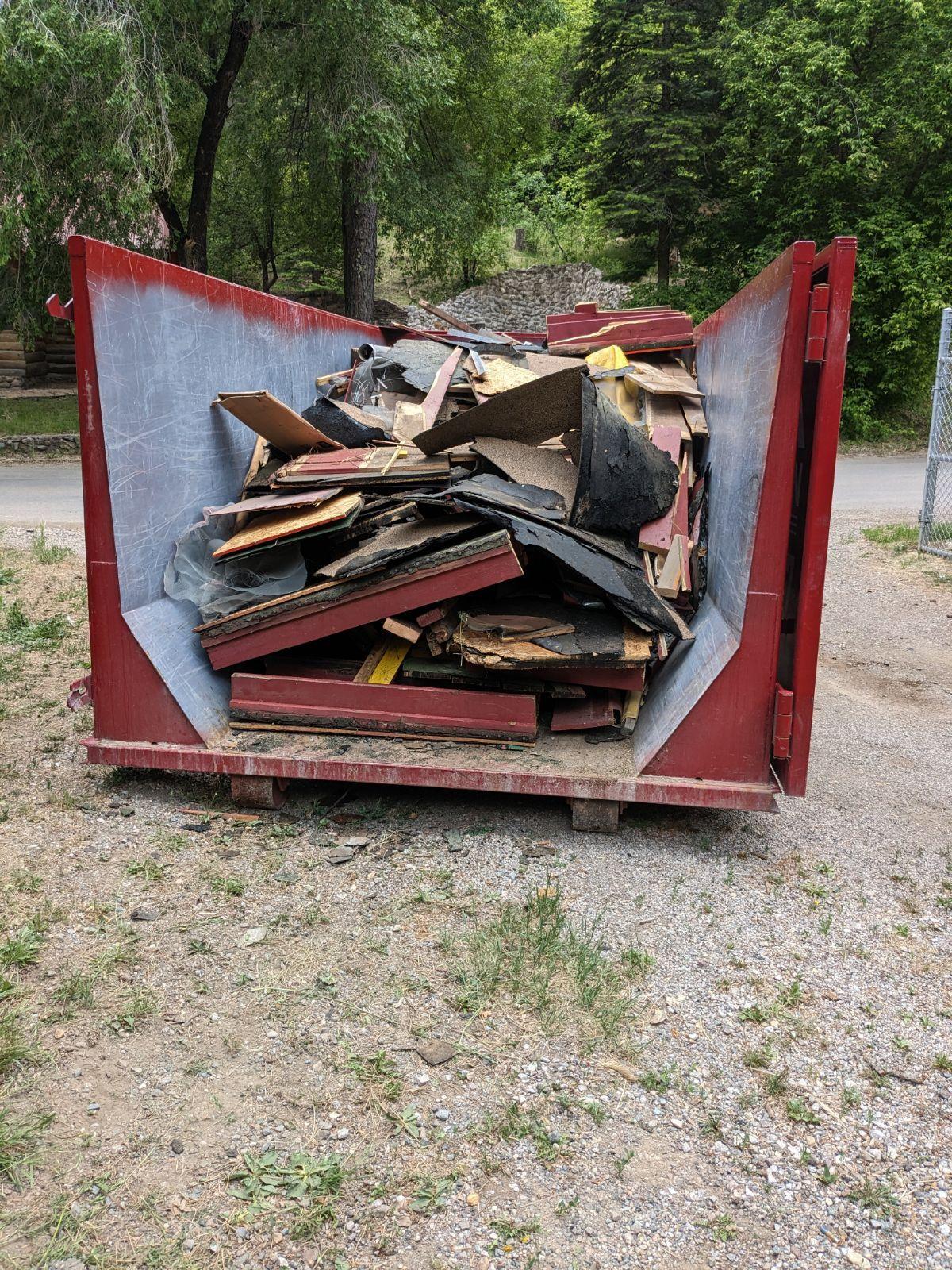 Large red open-top dumpster filled with wood and construction debris at a job site.