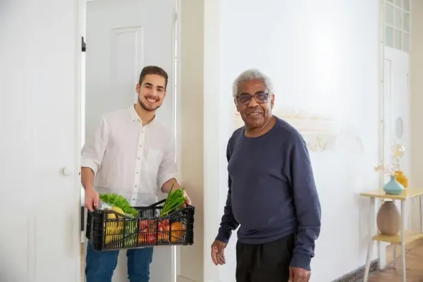 An home care professional bringing groceries to a man who is receiving elder care through Sumner In-Home Care and Preferred Care at Home