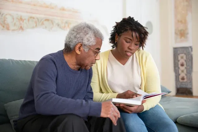 A female dementia caregiver reads to an elderly man with dementia. Specialized dementia care is provided by Sumner In-home Care and Preferred Care at Home