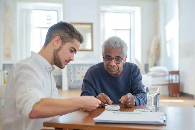 A male live-in caregiver helps an elderly man organize and schedule his medications. Live-in care is provided by Sumner In-home Care and Preferred Care at Home