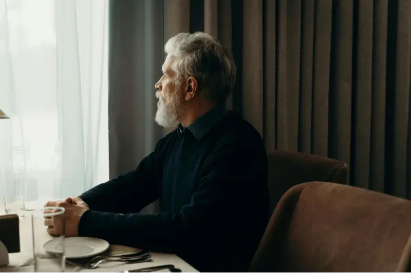 An elderly man sitting in a chair looking out the window, who is nearing the end of his transition care, as he has healed and does not need to be re-hospitalized, thanks to the transition care provided by Sumner In-home Care and Preferred Care at Home