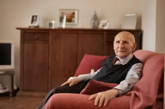 An elderly man sits in an arm chair smiling, knowing he is being taken care of 24/7 with the live-in care provided by Sumner In-home Care and Preferred Care at Home