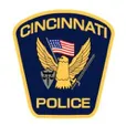 "Badge emblem of the Cincinnati Police, featuring a navy blue shield with a golden eagle perched on top, wings spread. Below the eagle, the American flag is draped across a shield displaying a medieval knight's helmet and a pair of crossed keys. The text 'CINCINNATI POLICE' is emblazoned at the top in bold, yellow letters on a blue background."