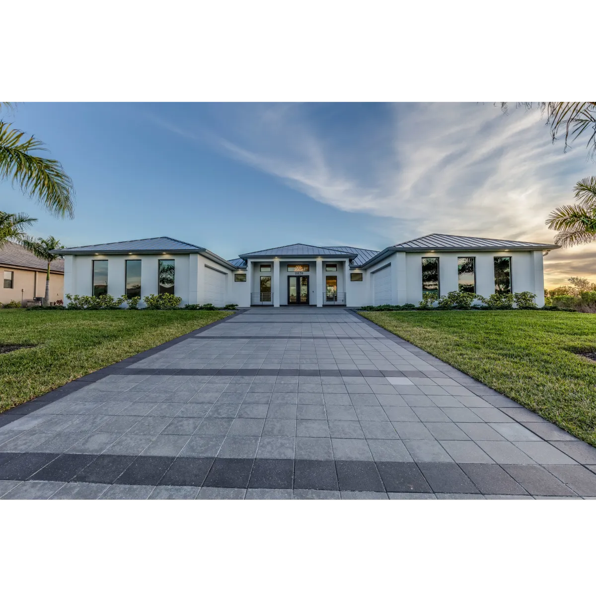 stone tile driveway leading to house made of grey stucco and 9 front facing windows 