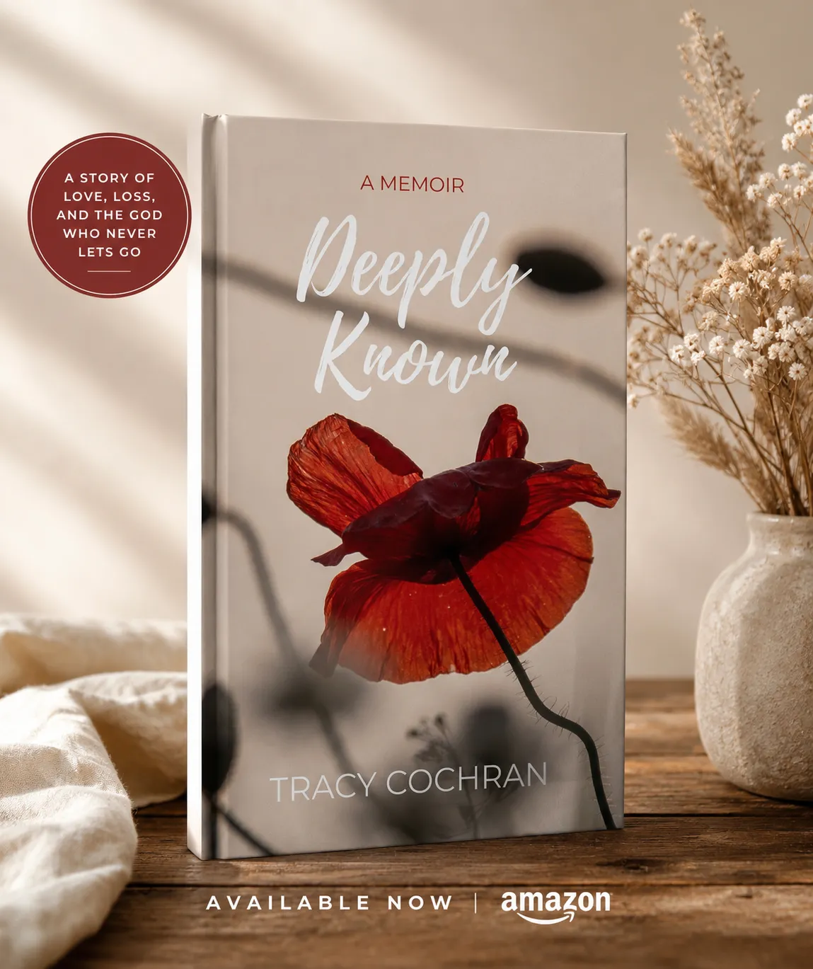 Hardcover copy of "Deeply Known: A Memoir" by Tracy Cochran standing on a wooden table beside dried flowers and a red poppy, with text reading "A story of love, loss, and the God who never lets go" and "Available now on Amazon."