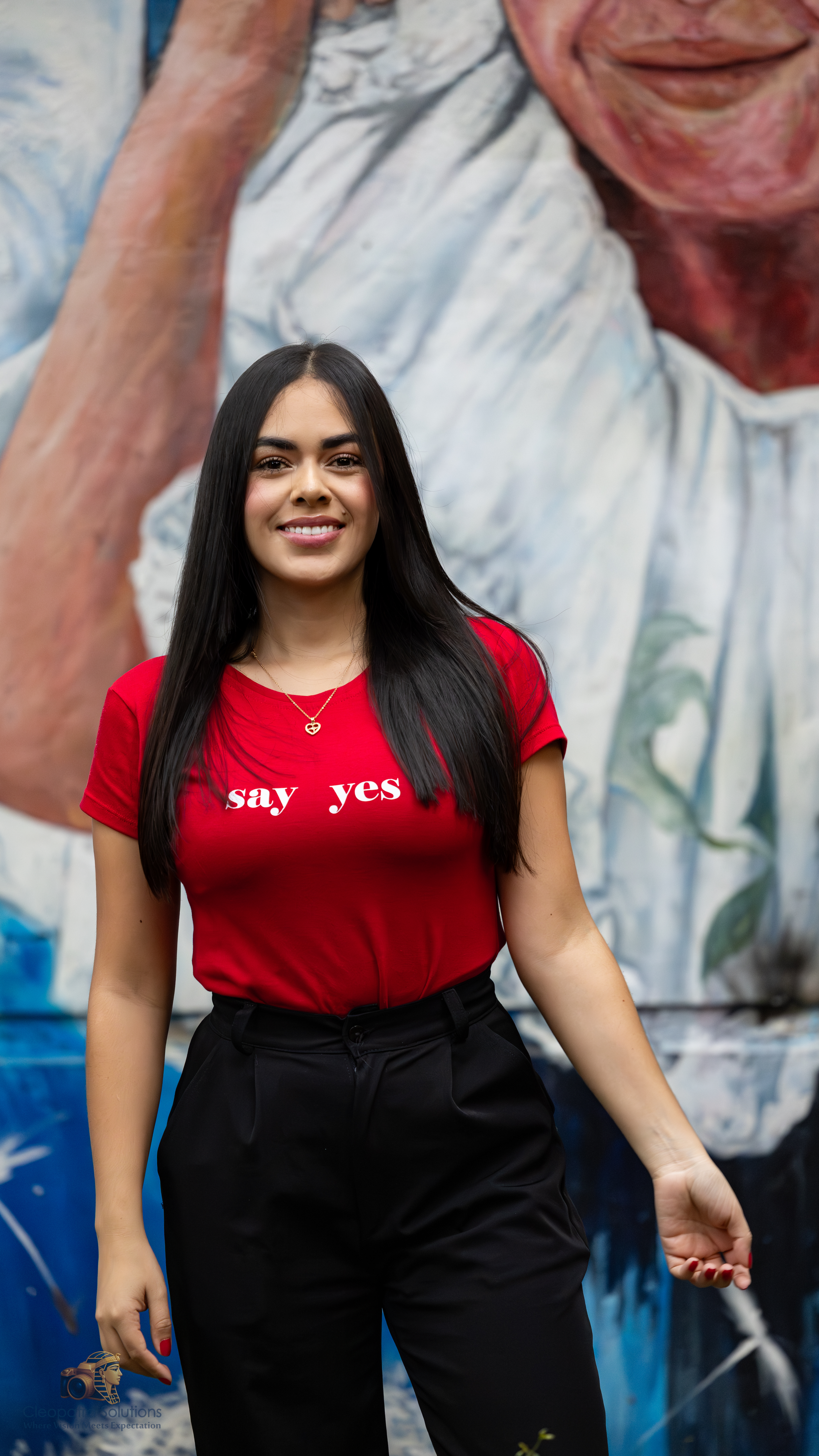 Woman smiling and posing in front of a colorful painted wall in an urban setting