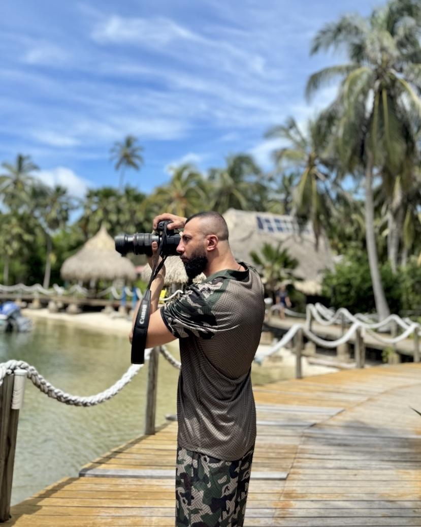 Photographer taking a picture with a professional camera on a wooden bridge surrounded by palm trees and tropical scenery