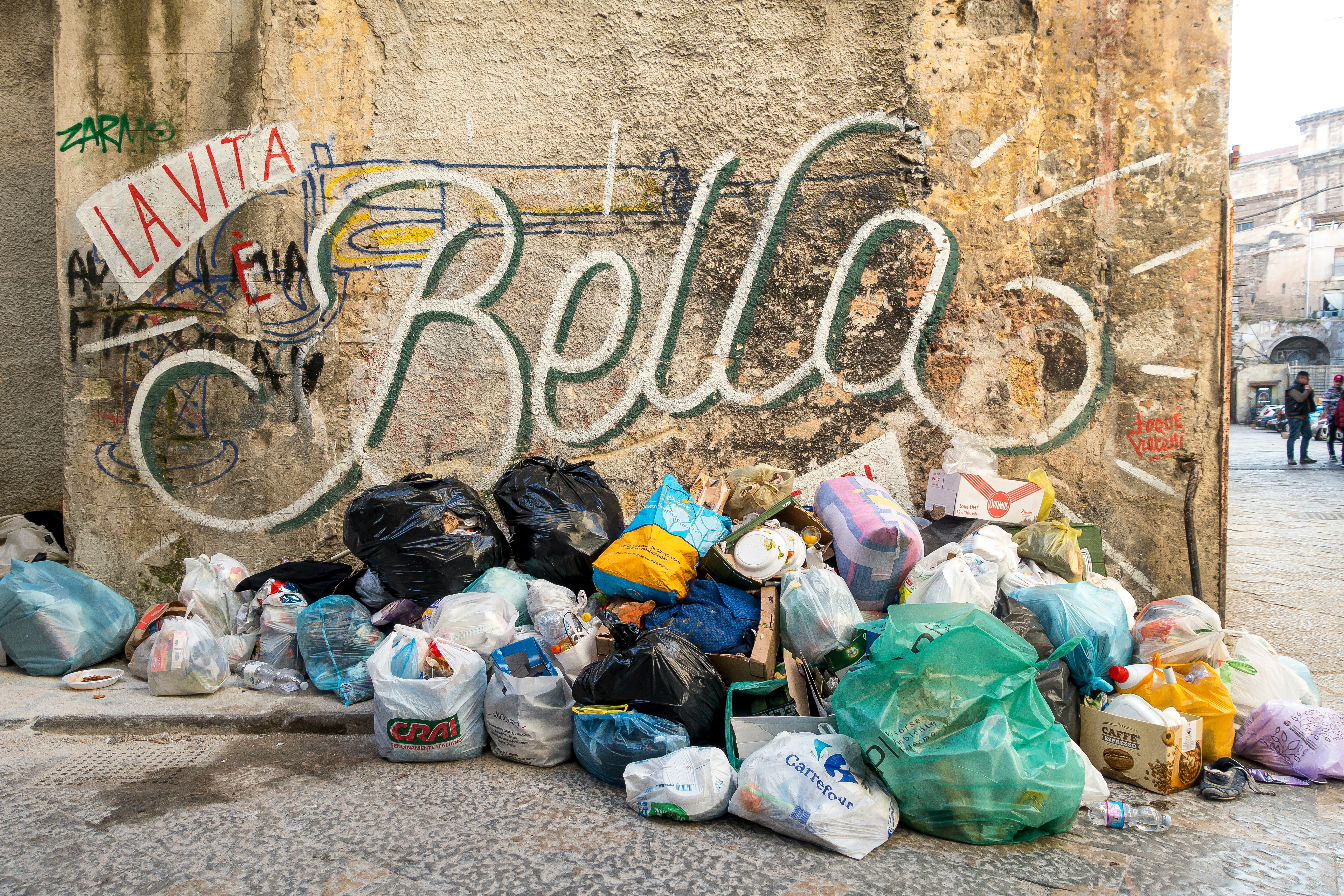 plastic bags left on side of street with a wall behind it