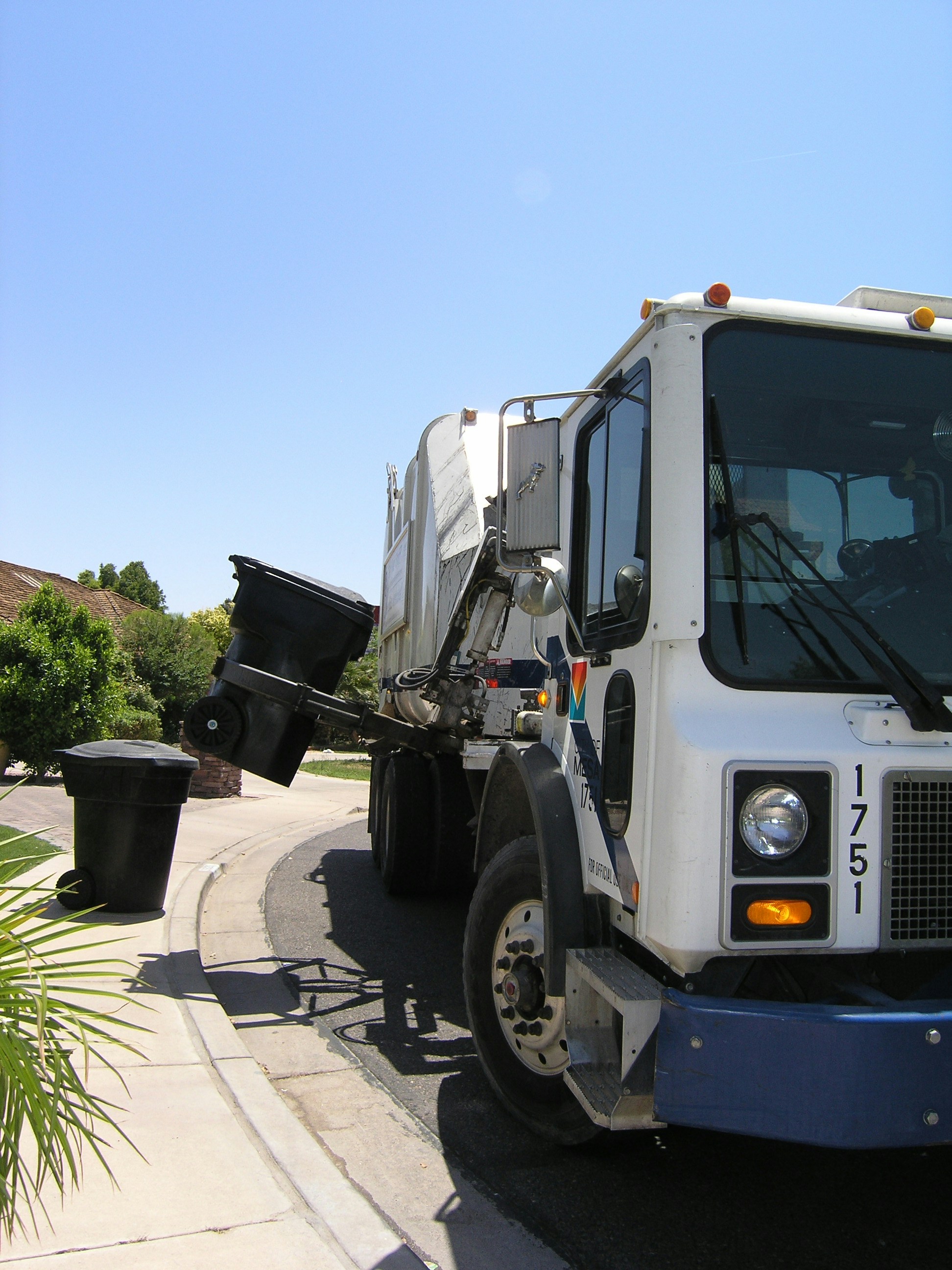 white truck using claws to take up bins from side of street