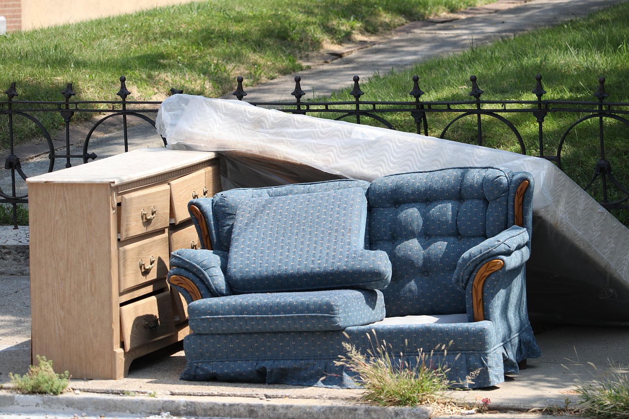 blue sofa, wooden cupboard and mattress lying outside with a fence behind it