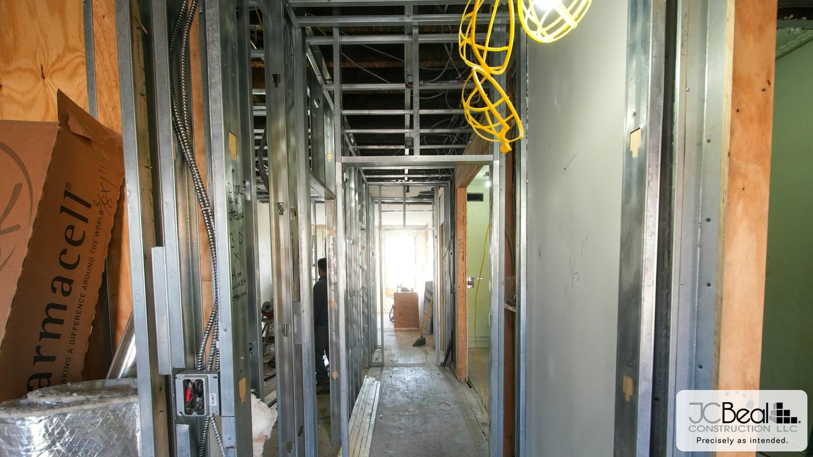 Interior hallway mid-renovation with exposed metal stud framing and a work light, JC Beal Construction logo overlay