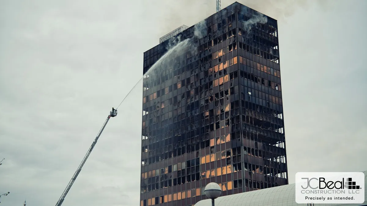 Firefighters directing a ladder-mounted master stream into the upper floors of a smoke-damaged commercial high-rise after a fire.