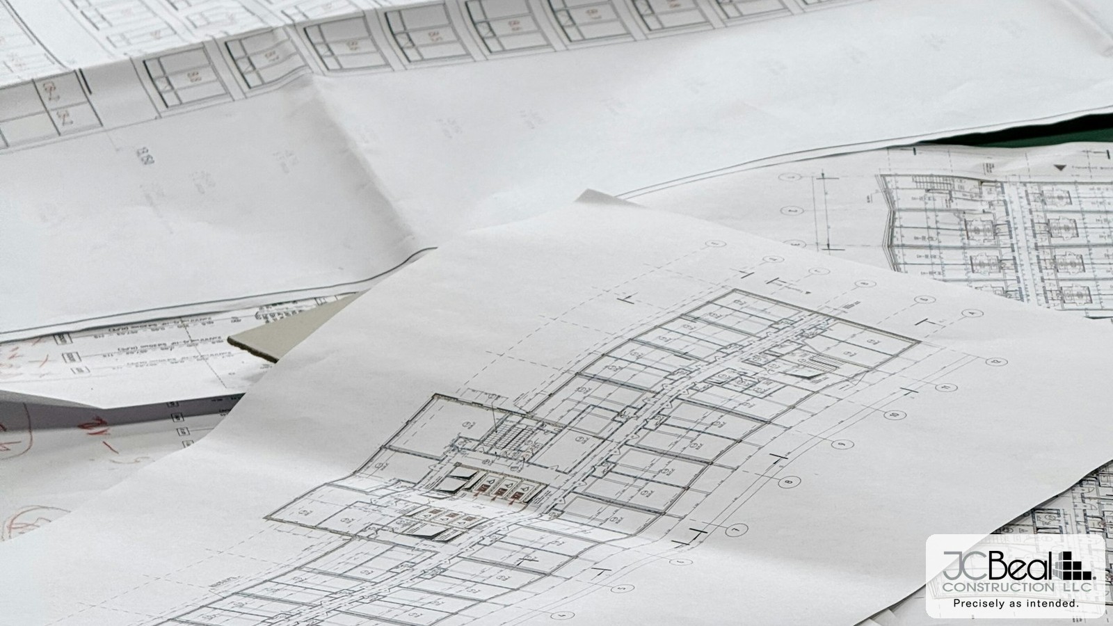 Architectural floor plans and building documents spread across a table, JC Beal Construction logo overlay