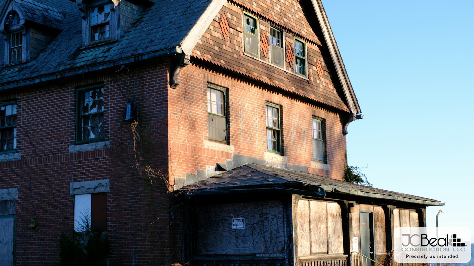 Vacant historic Victorian brick building with boarded first-floor windows and overgrown grounds, JC Beal Construction logo overlay