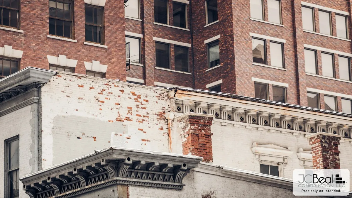 Weathered historic downtown brick building with repaired masonry and ornate cornice detail beside a modern office tower, JC Beal Construction